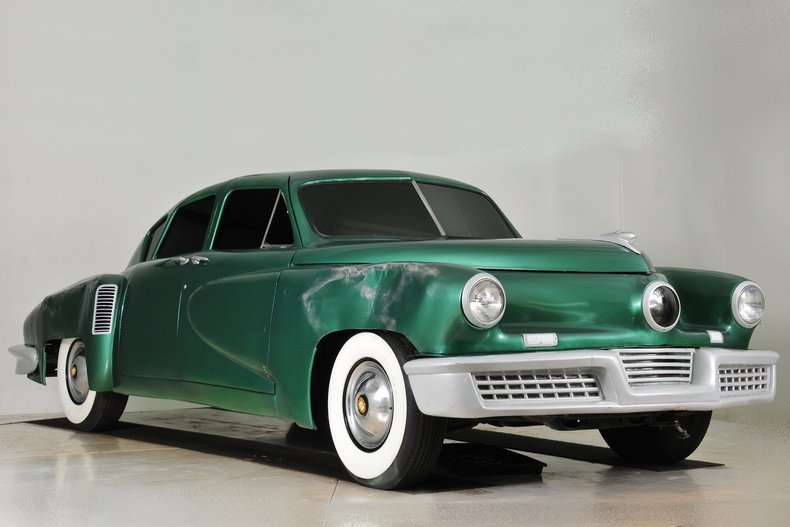 An image of the Tucker 48, a sleek and aerodynamic American automobile from 1948. Its distinctive design features include a wide front grille, pontoon fenders, and a centrally located third headlight that swivels with the steering.