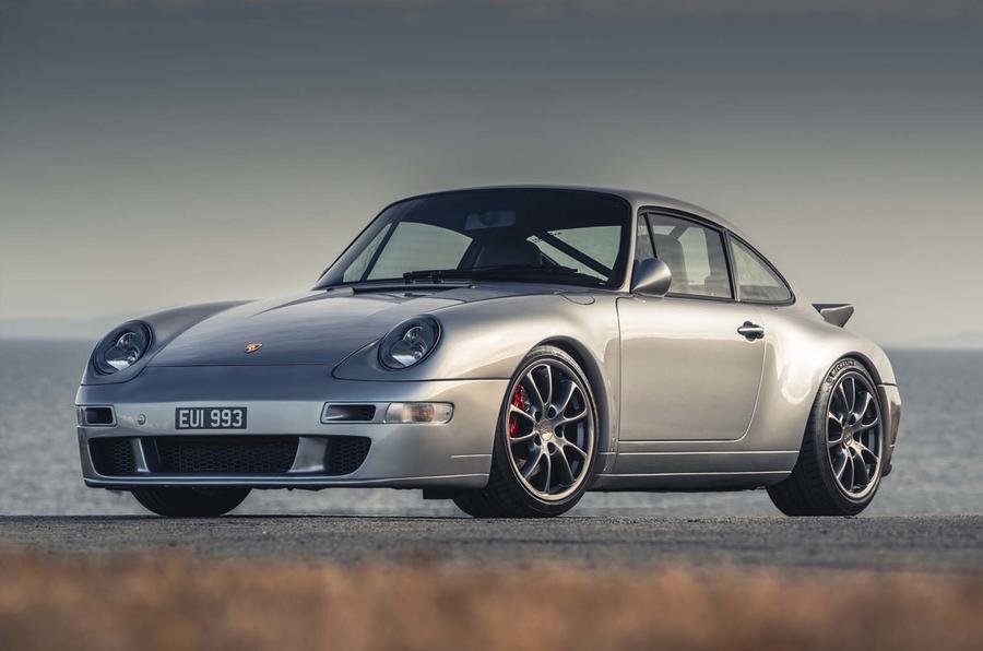 A silver Porsche 911 (993) parked on a scenic road, showcasing its sleek design and iconic curves under a clear blue sky.